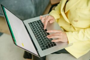 A person in a yellow jacket typing on a laptop indoors. Perfect for depicting work from home or business scenarios.